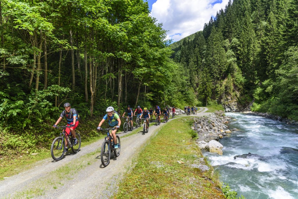 eine Gruppe Mountainbiker fährt an einem Wildbach in den Alpen entlang aufwärts